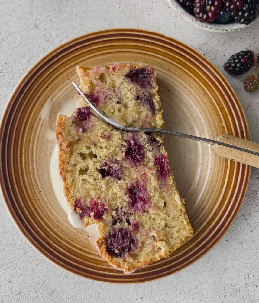 Slice of moist vegan pound cake showcasing a tangy lemon glaze and vibrant blackberries."